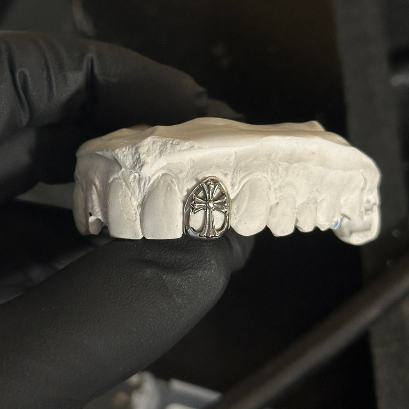 dental silver chrome cross grillz on a white stone model being held by a black glove