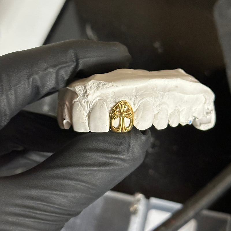 Dental gold chrome cross cap on a white stone mould being held  by a black glove