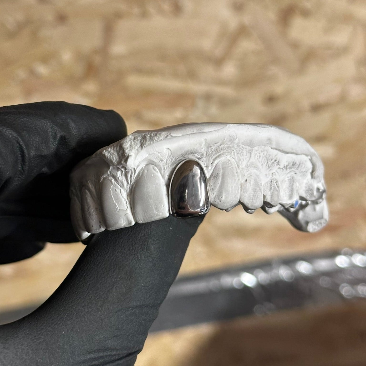 Dental Silver Grill , 1 cap on a stone mould held in the air by a black glove