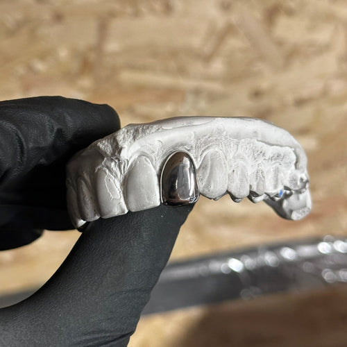 Dental Silver Grill , 1 cap on a stone mould held in the air by a black glove